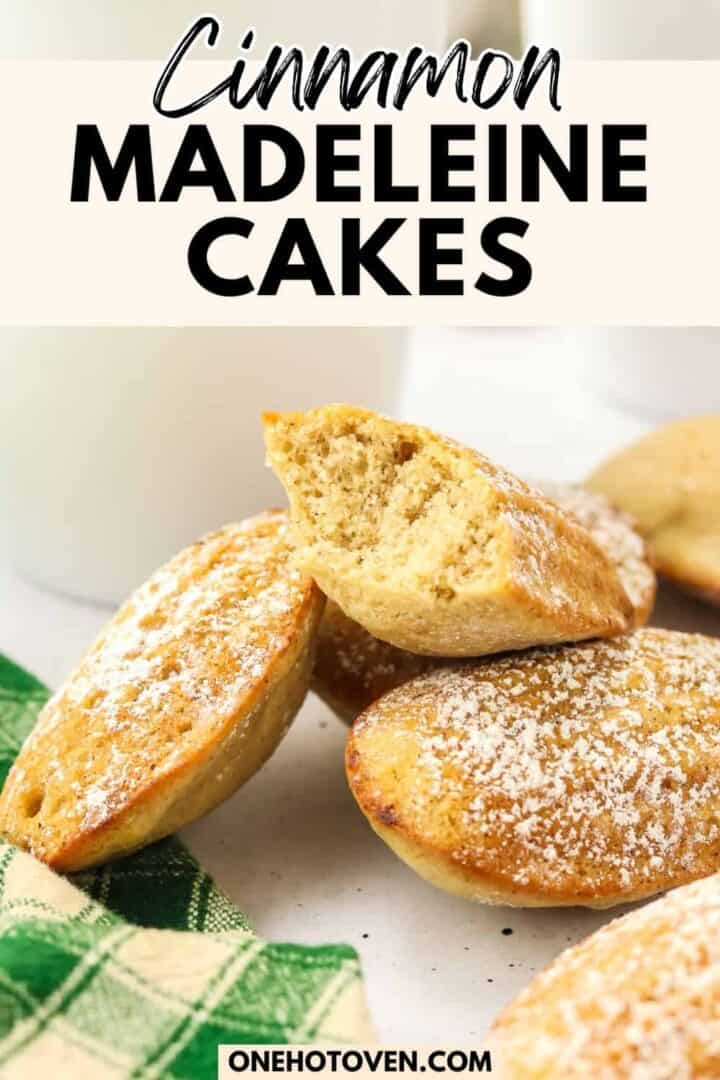 A plate of cinnamon madeleine cakes dusted with powdered sugar, with one cake broken in half, next to a green checkered cloth.