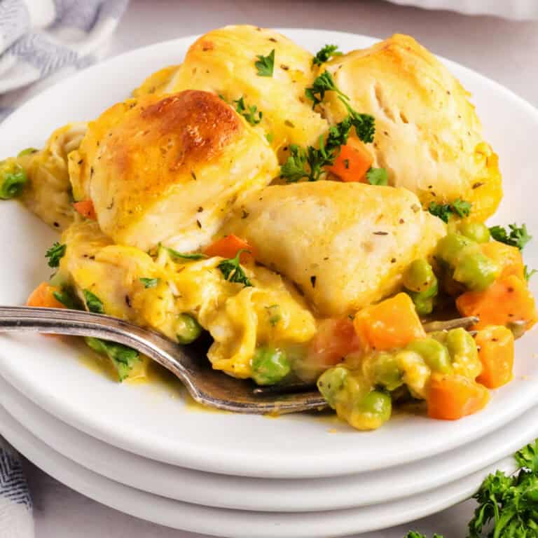 A plate of biscuit-topped vegetable pot pie with carrots, peas, and a creamy sauce, garnished with chopped parsley, and a fork on the side.