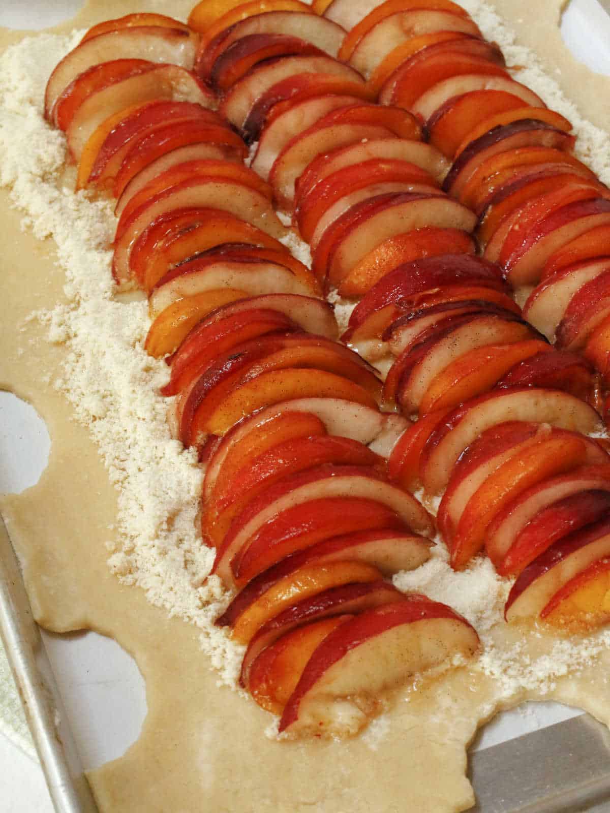 Rows of sliced plums are neatly arranged on a rectangular sheet of pastry dough with a layer of crumb filling underneath, ready to be baked.