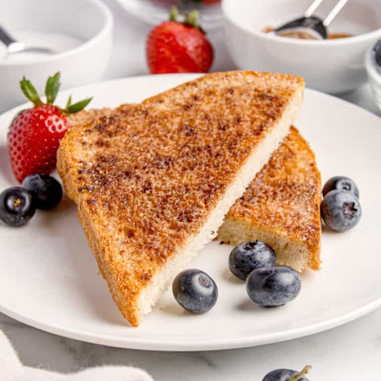 Two slices of broiled cinnamon toast on a white plate, garnished with fresh strawberries and blueberries.