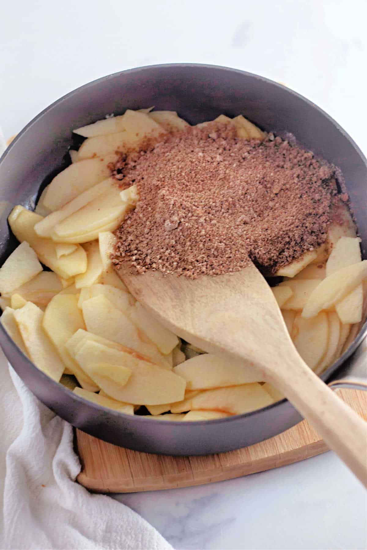 Sliced apples in a skillet topped with a brown sugar, being stirred with a wooden spoon.