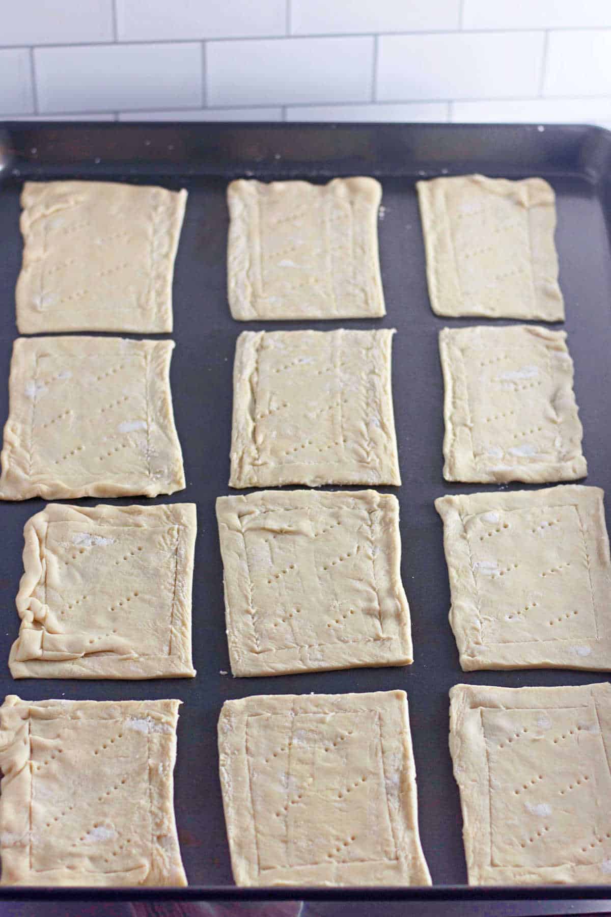 Twelve rectangular pieces of unbaked pastry dough arranged in a grid on a baking sheet.
