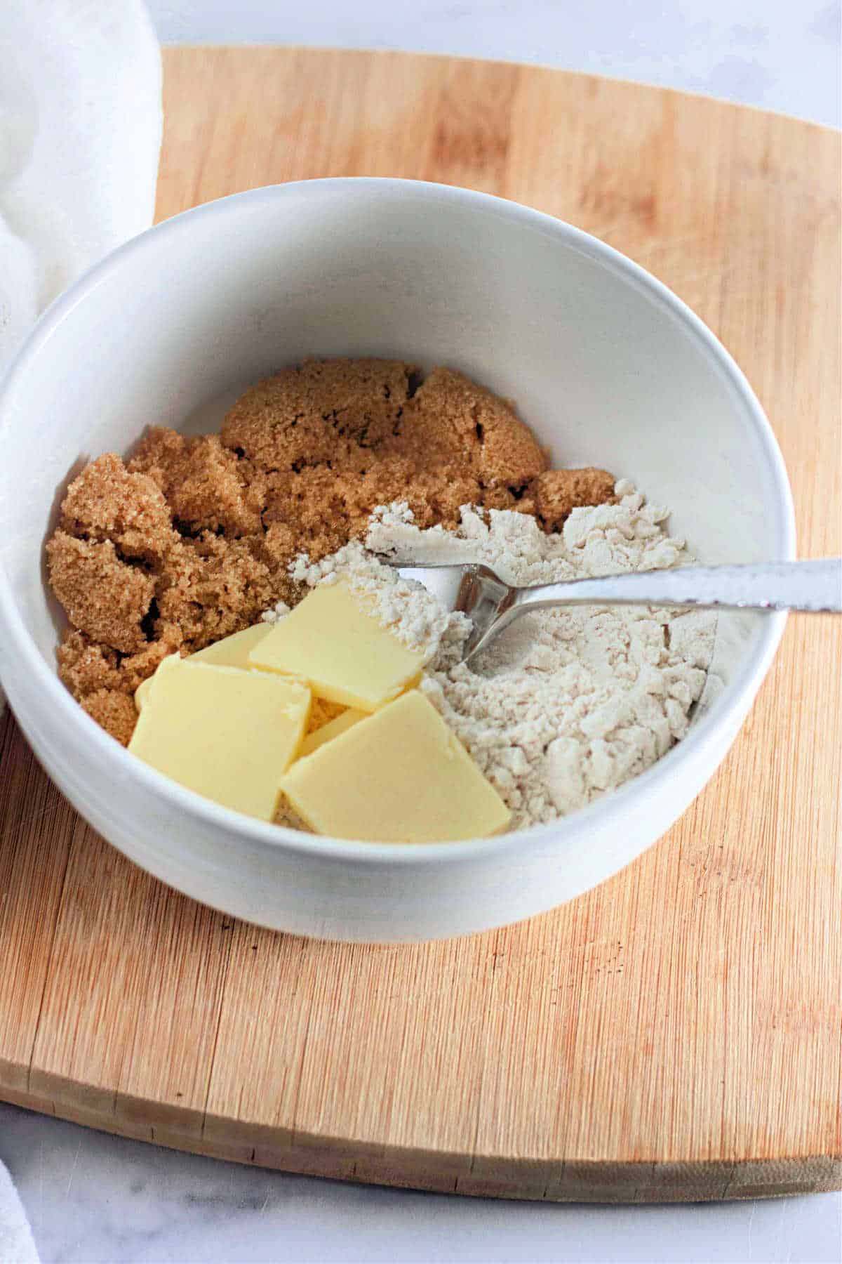 A white bowl containing brown sugar, flour, and butter cubes with a fork for a streusel topping.