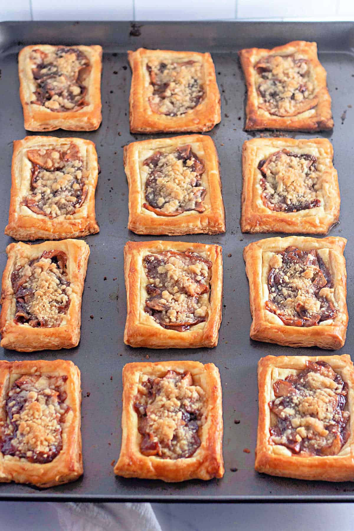 A baking sheet lined with twelve rectangular apple pastries topped with crumble.