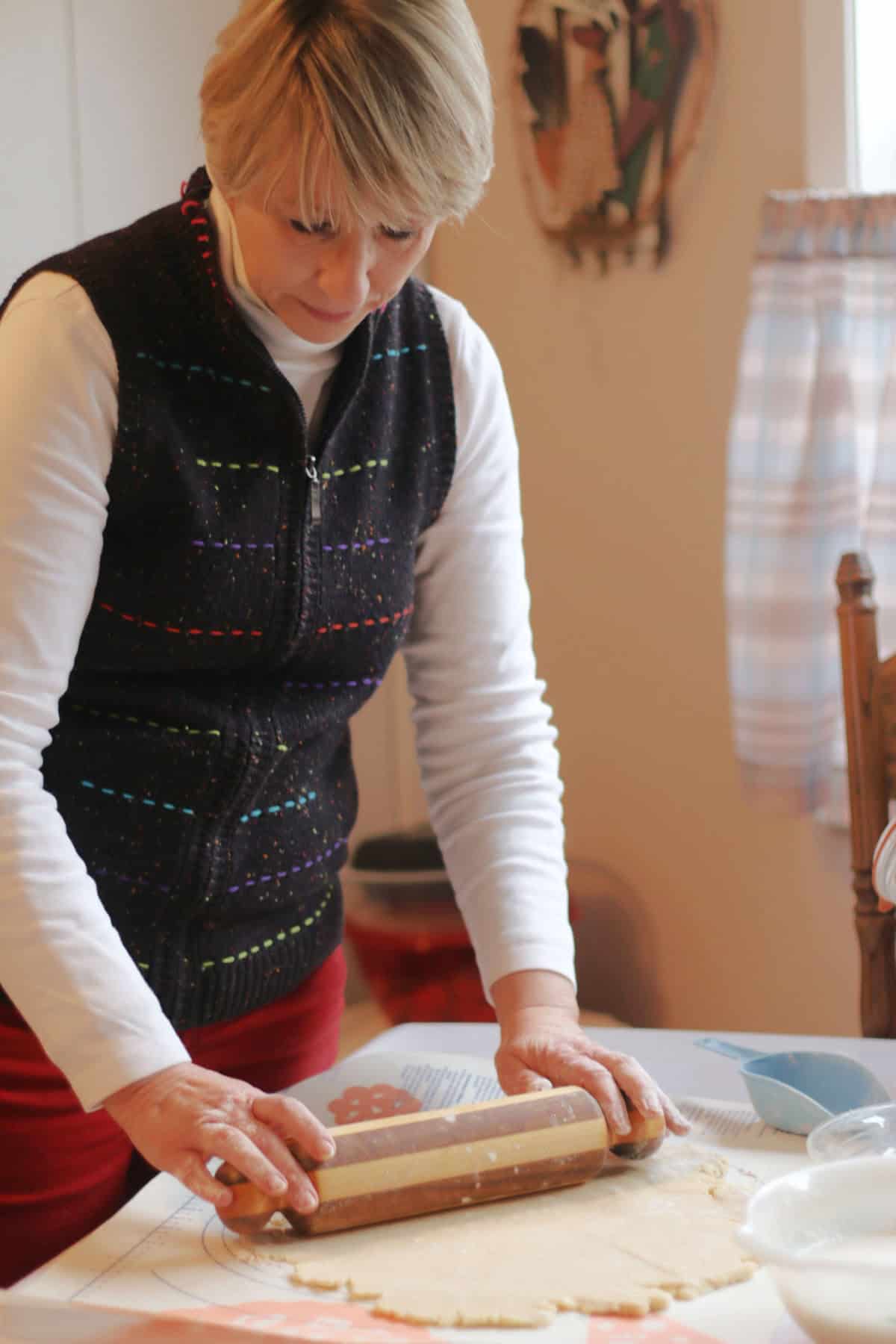 A Jere Cassidy uses a rolling pin to flatten dough on a floured surface in a kitchen.