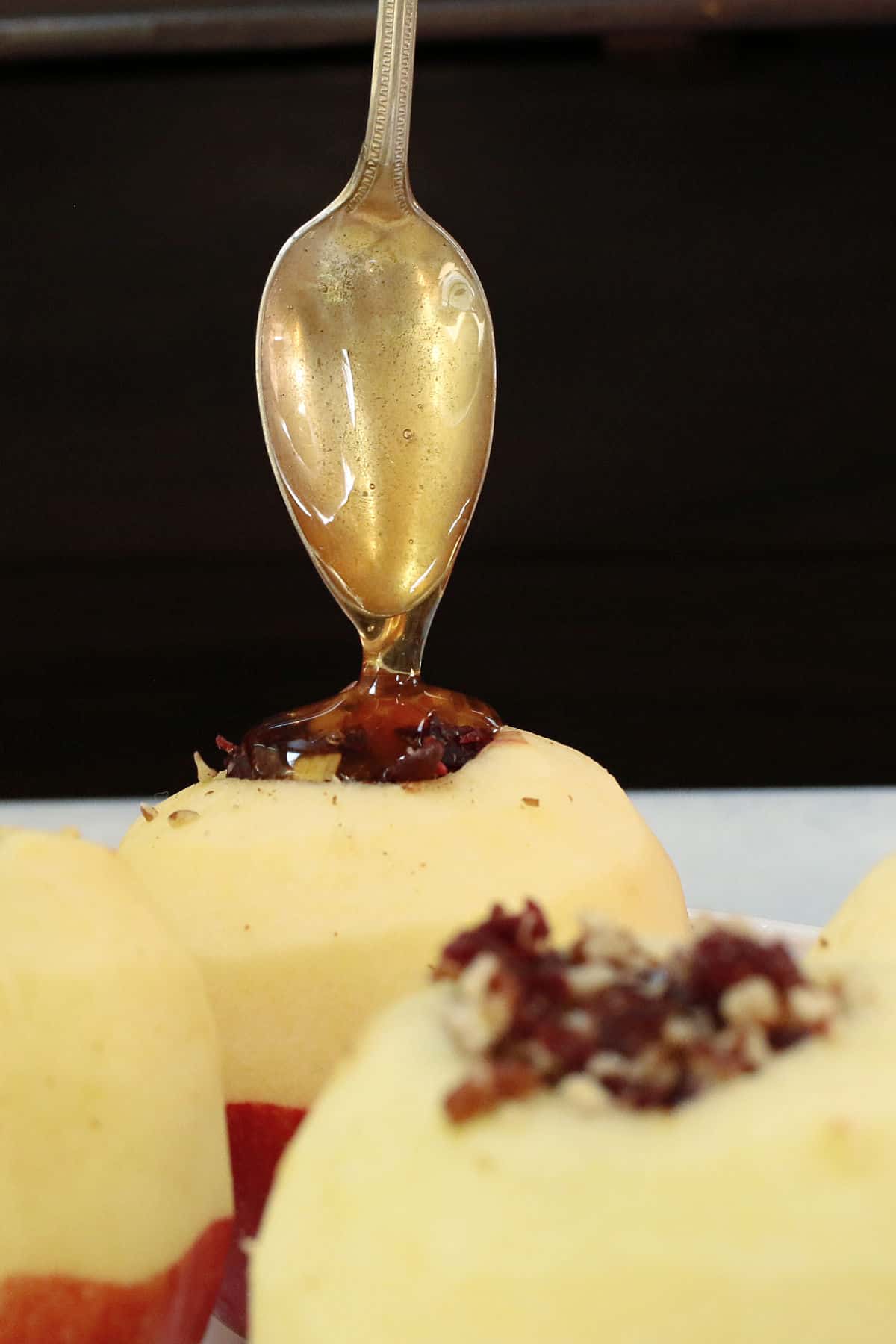 A spoon drizzles honey over a peeled apple stuffed with dried fruit and nuts.