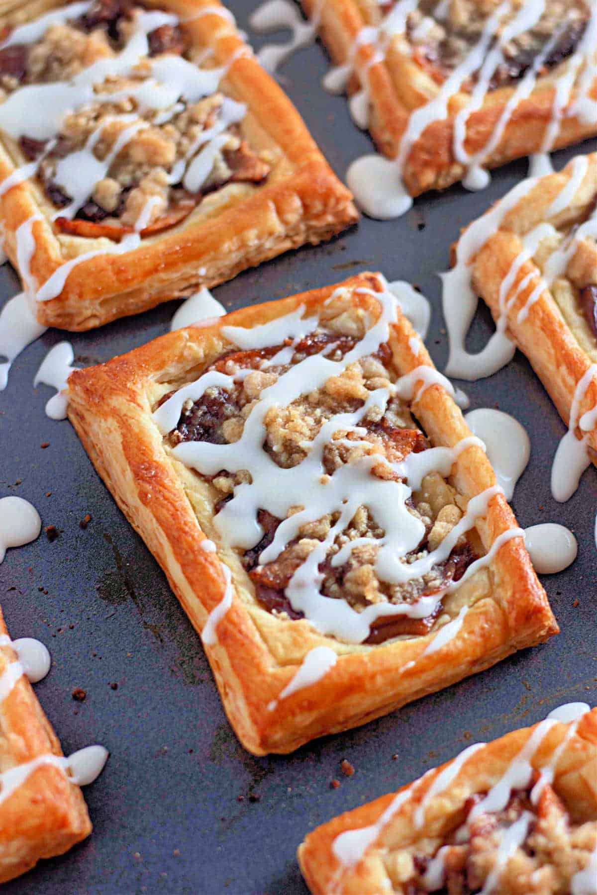 Rectangular aplled-filled puff pastries drizzled with white icing on a baking sheet.