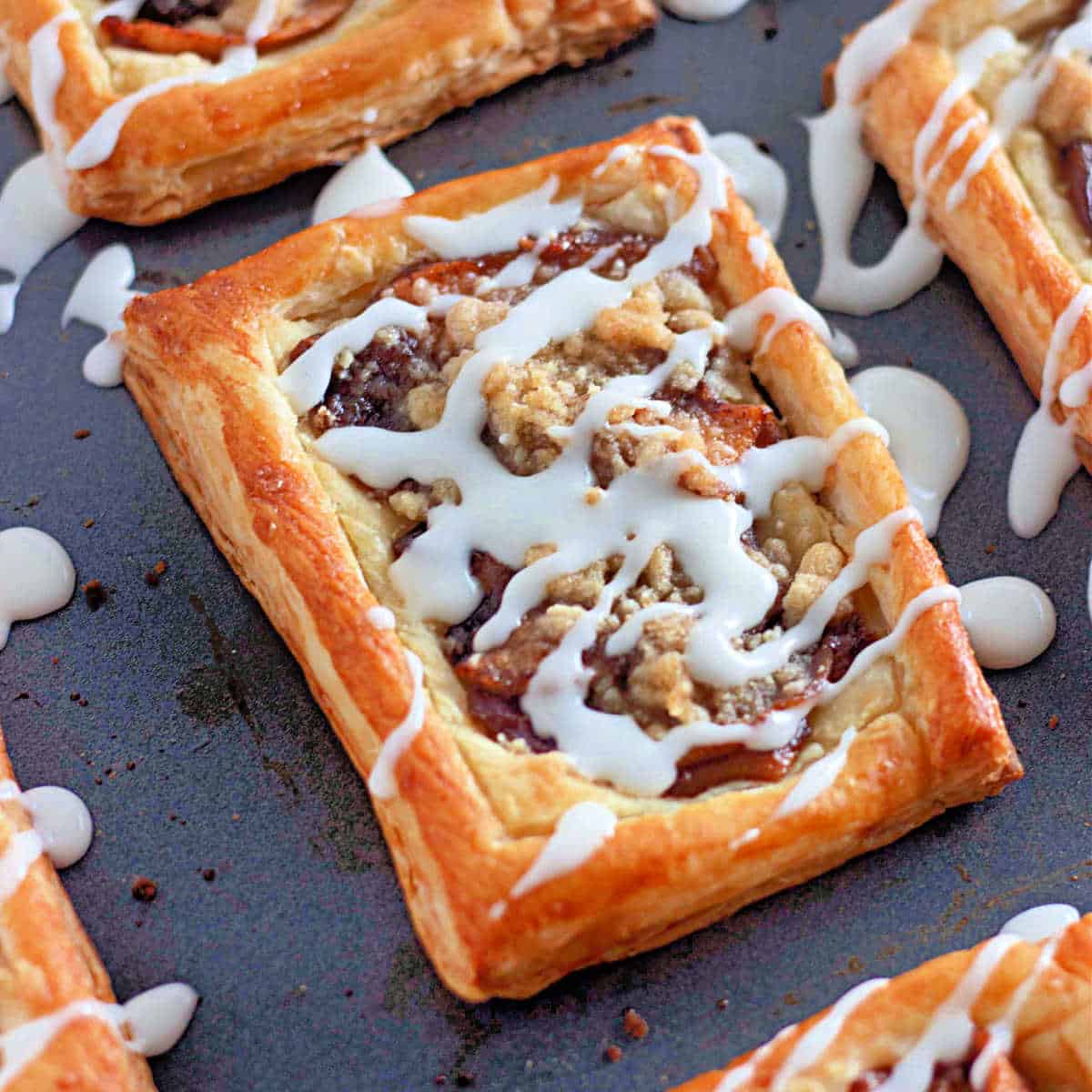 A rectangular apple pastry topped with streusel and white icing on a baking sheet.