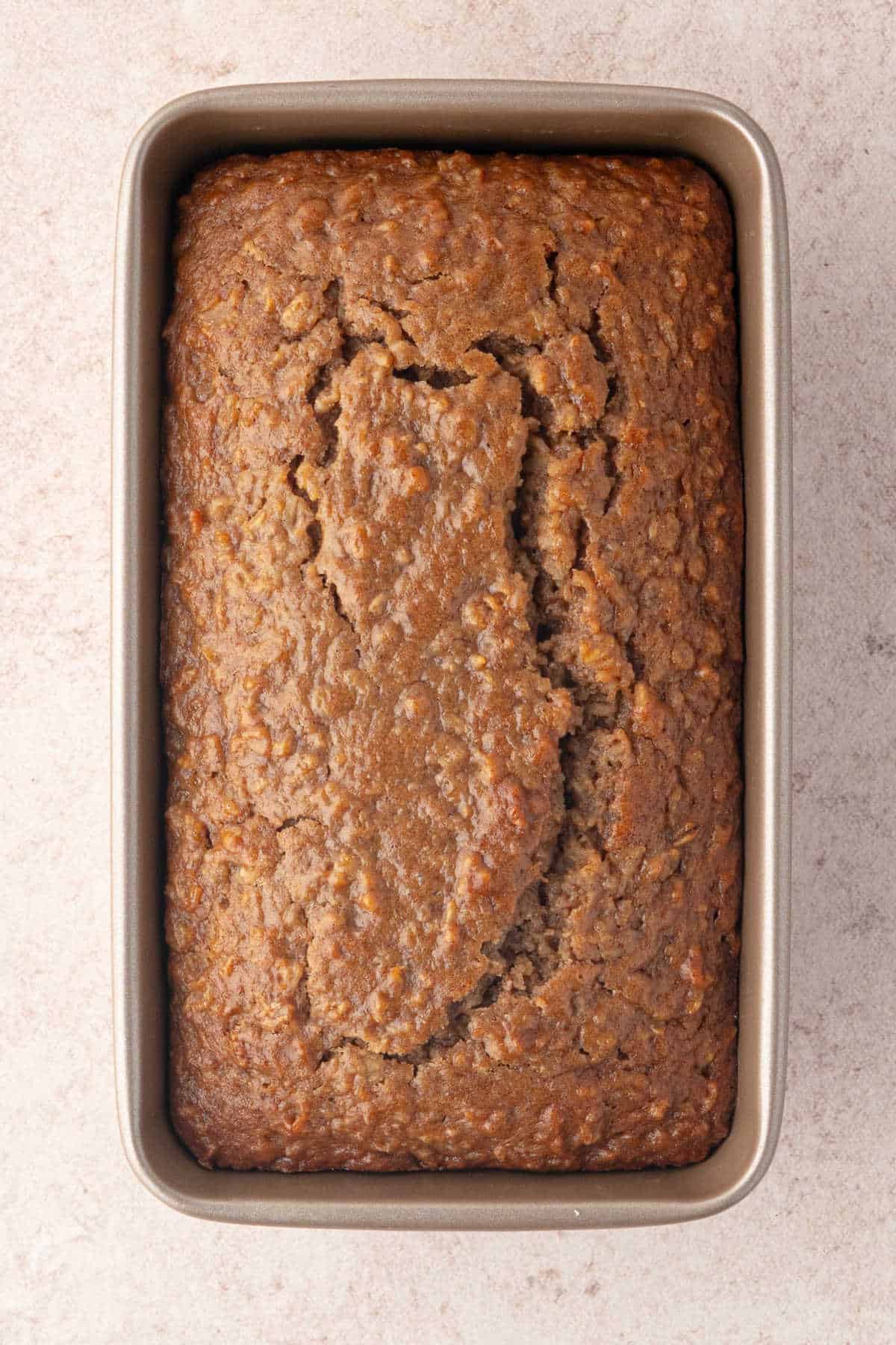 A loaf of baked oatmeal bread in a rectangular metal pan.