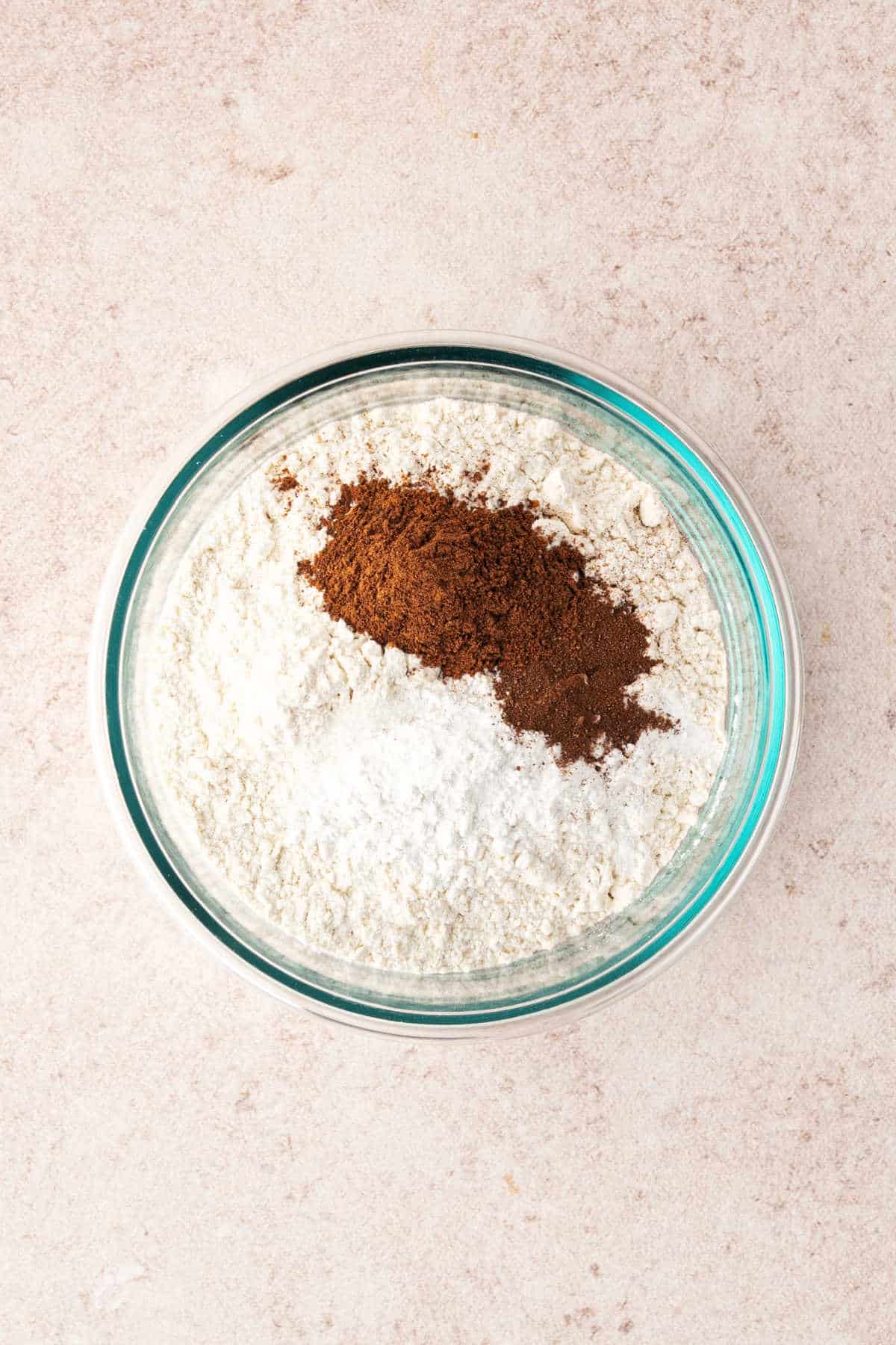 A glass bowl containing flour, baking powder, and a pile of cinnamon.