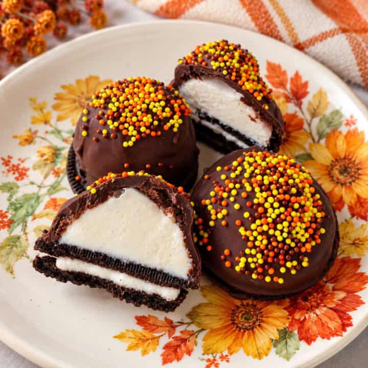Four chocolate-covered Oreo ice cream bites topped with orange and yellow sprinkles on a floral plate