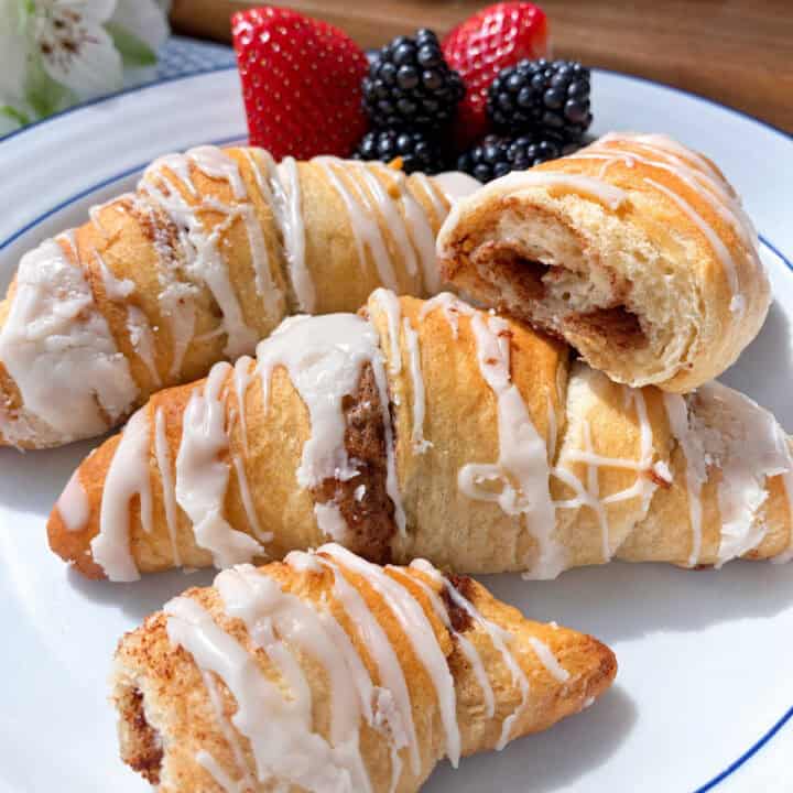Glazed cinnamon crescent rolls on a plate with strawberries and blackberries.