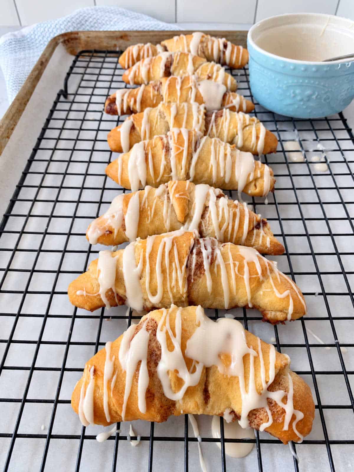 Seven crescent roll cinnamon rolls drizzled with white icing, arranged in a row on a wire cooling rack.