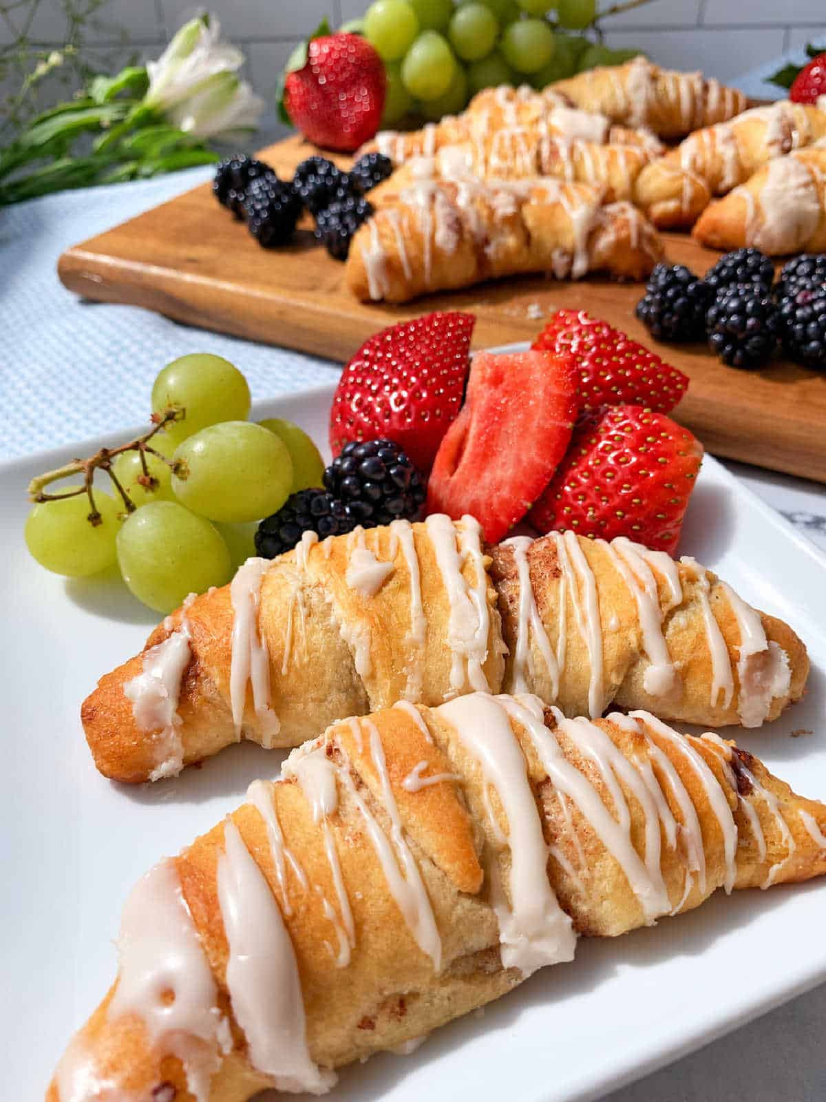 Two glazed, crescent-shaped pastries on a white plate with fresh strawberries, blackberries, and green grapes.