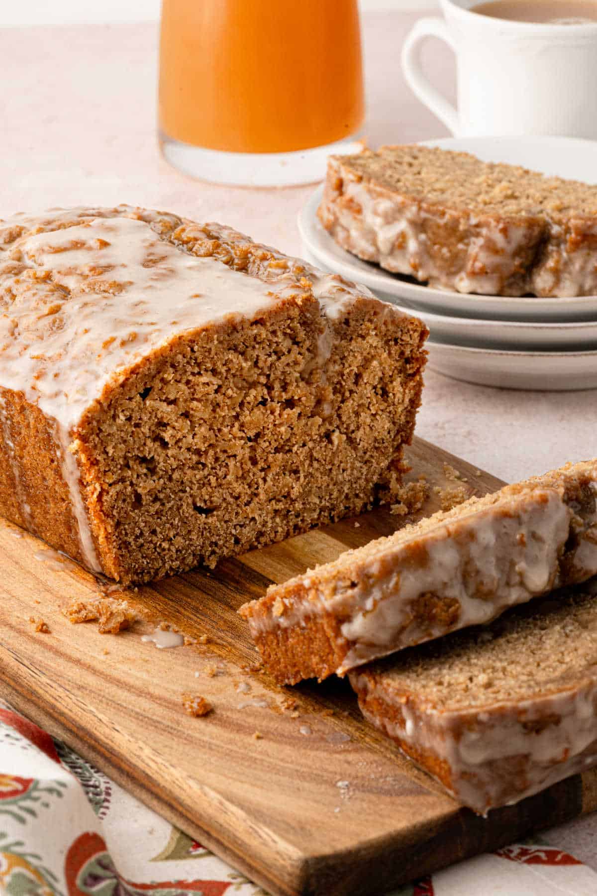 A glazed loaf of spiced bread on a wooden board, with several slices cut and a plate of more slices in the background.