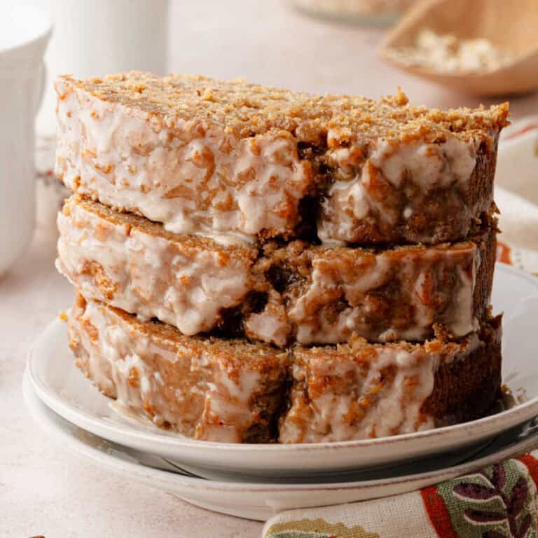 A stack of three thick slices of glazed oatmeal bread on a white plate.